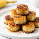 Pan Fried Cinnamon Bananas golden and caramelized on a white plate dusted with powdered sugar