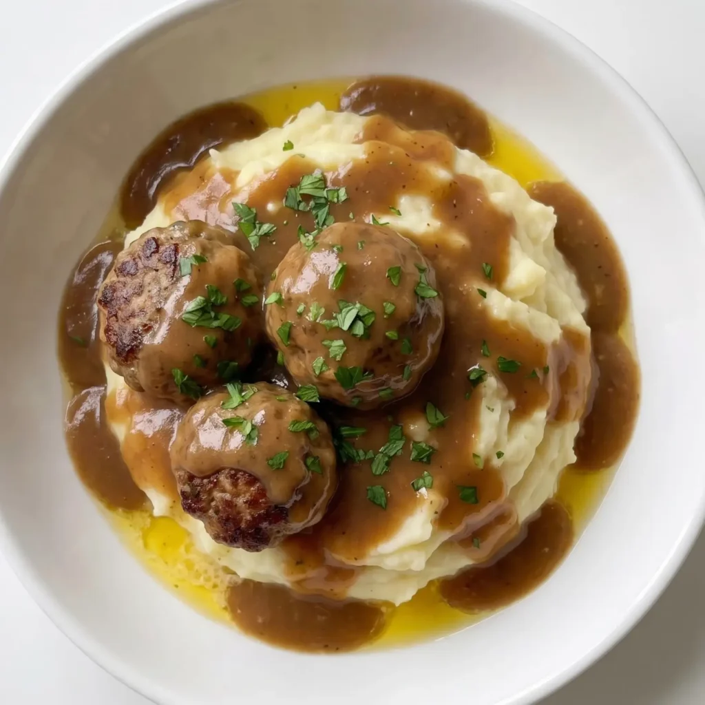 Juicy meatballs served over creamy mashed potatoes with pan sauce and fresh parsley on a white plate