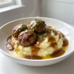 Juicy meatballs served over creamy mashed potatoes with pan sauce and fresh parsley on a white plate